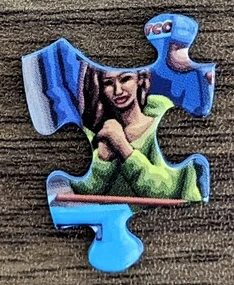 Photograph of a loose blue jigsaw piece showing a woman in green, on a wooden surface.